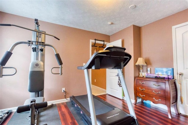 exercise area featuring baseboards, wood finished floors, and a textured ceiling