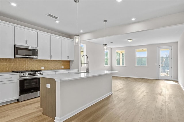 kitchen featuring a sink, stainless steel appliances, a center island with sink, light wood-style flooring, and decorative backsplash