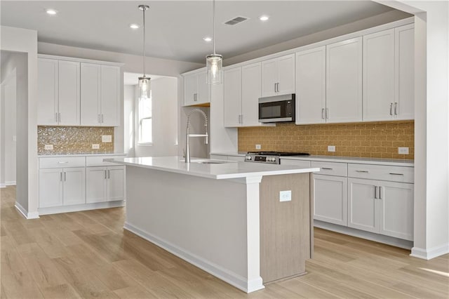 kitchen with stainless steel microwave, light wood-style flooring, a sink, and an island with sink