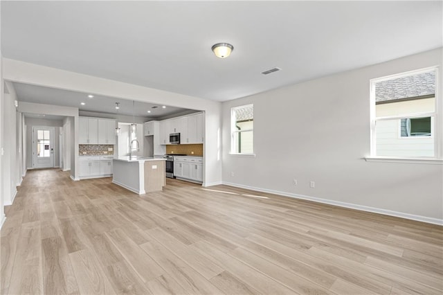 unfurnished living room featuring a sink, visible vents, recessed lighting, baseboards, and light wood-style floors