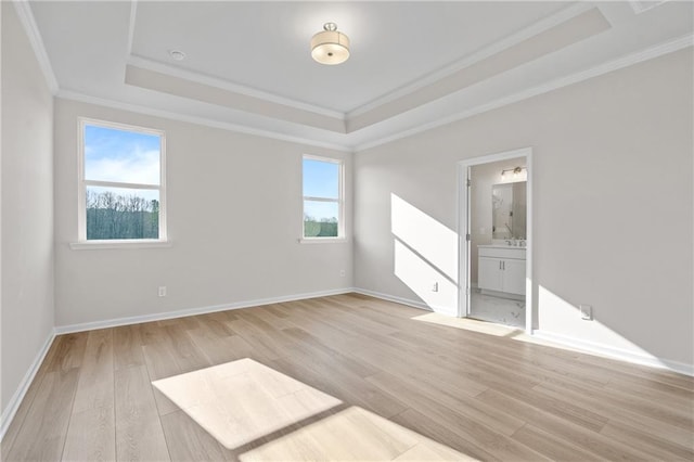 spare room featuring a tray ceiling, crown molding, baseboards, and light wood-type flooring