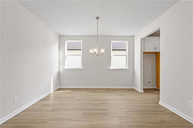 unfurnished dining area featuring light wood finished floors, an inviting chandelier, and baseboards