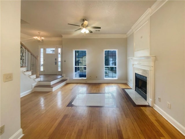 unfurnished living room with ceiling fan with notable chandelier, a wealth of natural light, a premium fireplace, and light wood-type flooring