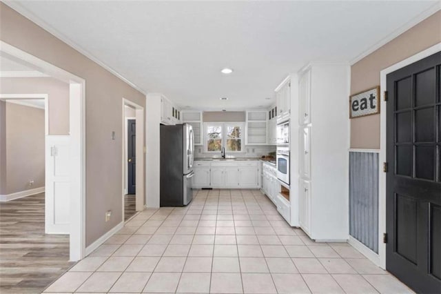 kitchen with white cabinets, ornamental molding, appliances with stainless steel finishes, a sink, and light tile patterned flooring