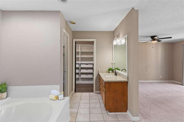 bathroom with ceiling fan, tile patterned flooring, a spacious closet, vanity, and a bath