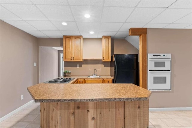 kitchen with white double oven, freestanding refrigerator, stainless steel stovetop, light countertops, and a sink