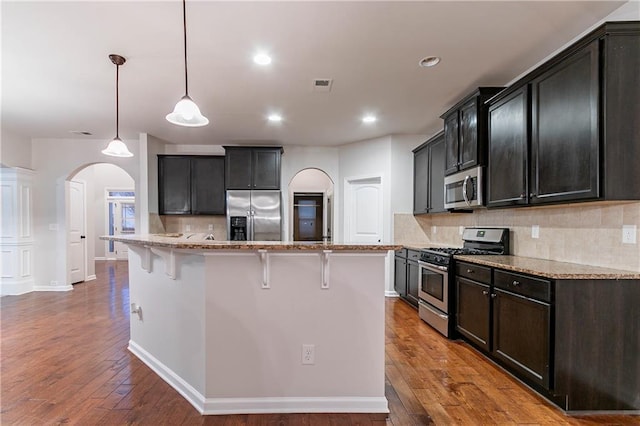 kitchen featuring appliances with stainless steel finishes, hanging light fixtures, light stone counters, a center island, and a kitchen bar