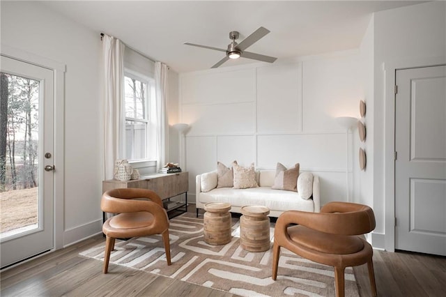 sitting room with wood finished floors, a ceiling fan, and a decorative wall