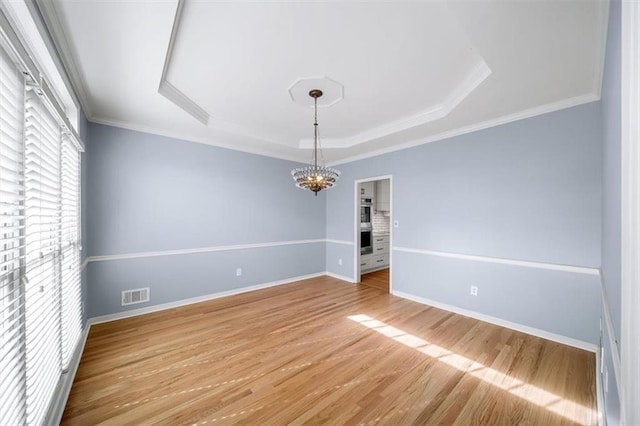 unfurnished dining area featuring a raised ceiling, crown molding, hardwood / wood-style floors, and an inviting chandelier