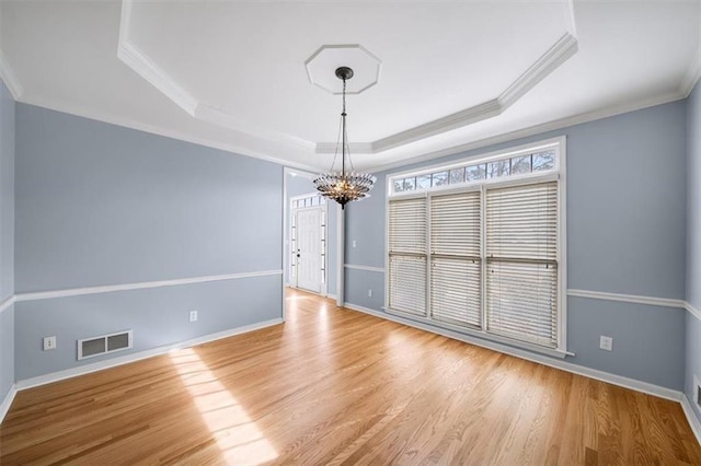 spare room featuring a raised ceiling, crown molding, a notable chandelier, and light wood-type flooring