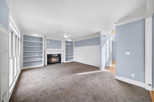 unfurnished living room featuring built in features, carpet flooring, ceiling fan, a high end fireplace, and crown molding