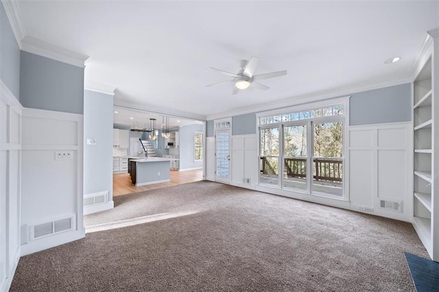 unfurnished living room featuring ceiling fan, a healthy amount of sunlight, ornamental molding, and light colored carpet