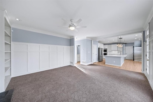 unfurnished living room featuring sink, ornamental molding, light colored carpet, and ceiling fan