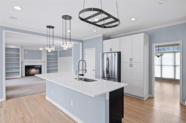 kitchen featuring pendant lighting, white cabinetry, sink, stainless steel fridge, and a center island with sink