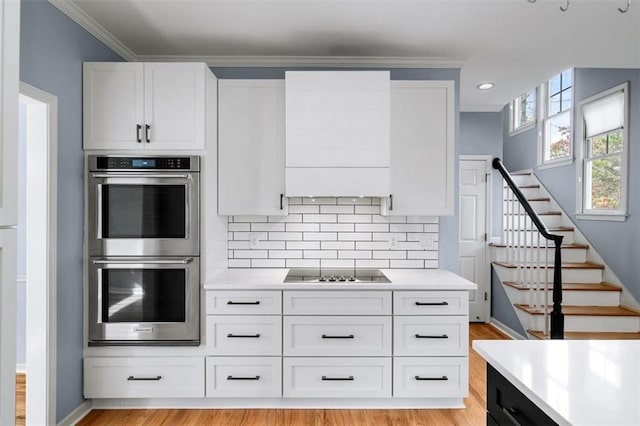 kitchen featuring black electric cooktop, backsplash, double oven, and white cabinets