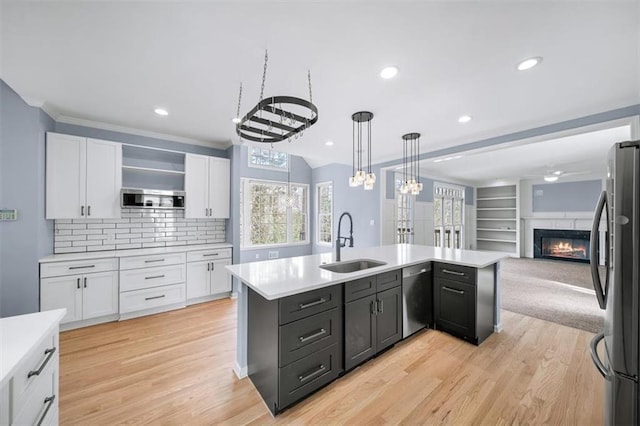 kitchen featuring pendant lighting, sink, appliances with stainless steel finishes, white cabinetry, and a center island with sink