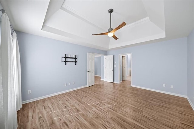 unfurnished bedroom featuring a tray ceiling, ensuite bathroom, ceiling fan, and light wood-type flooring