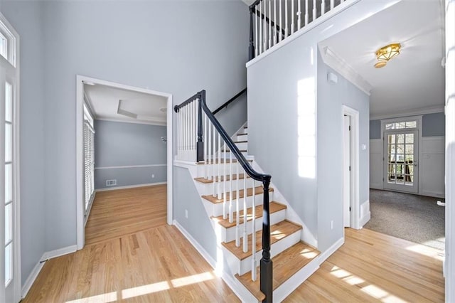 staircase with wood-type flooring, ornamental molding, and a towering ceiling