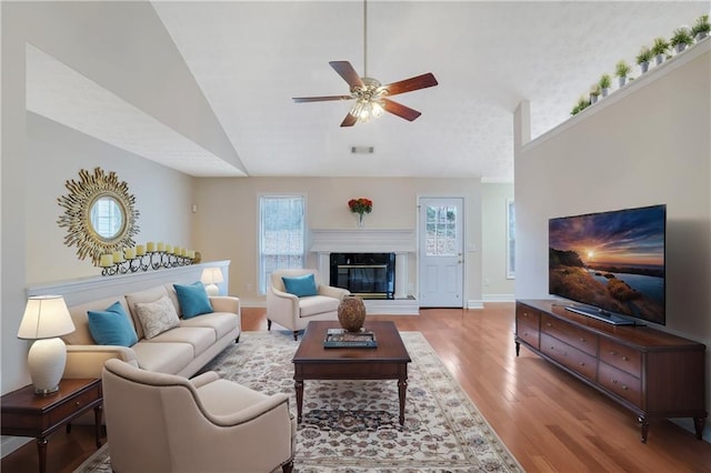 living room featuring ceiling fan, a high end fireplace, light hardwood / wood-style flooring, and vaulted ceiling