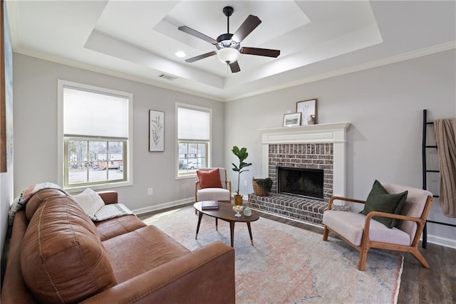 living area featuring a tray ceiling, a brick fireplace, wood finished floors, and baseboards