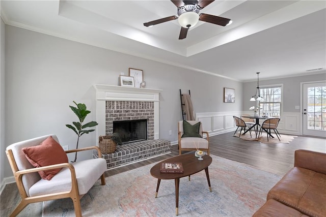 living room featuring ornamental molding, wood finished floors, wainscoting, and a raised ceiling