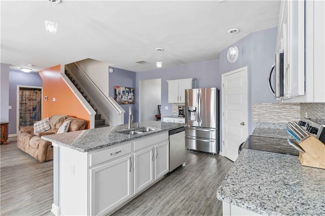 kitchen with stainless steel appliances, an island with sink, hanging light fixtures, and white cabinets