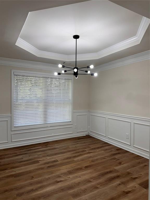 unfurnished room with an inviting chandelier, a tray ceiling, dark wood-type flooring, and ornamental molding