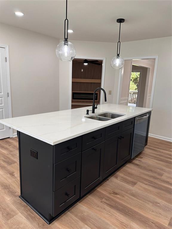 kitchen featuring a kitchen island with sink, sink, decorative light fixtures, and stainless steel dishwasher