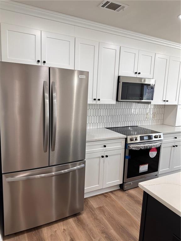 kitchen with tasteful backsplash, light stone counters, appliances with stainless steel finishes, light hardwood / wood-style floors, and white cabinets