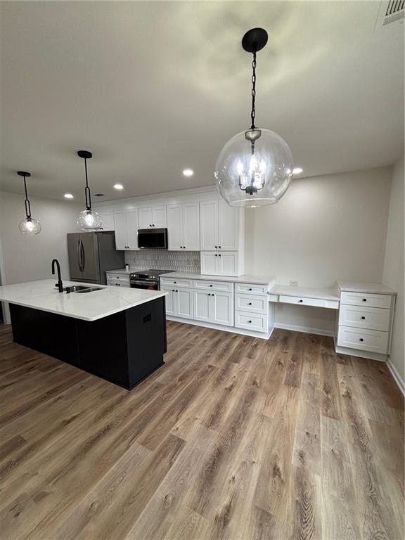 kitchen with a spacious island, white cabinetry, decorative light fixtures, stainless steel appliances, and light hardwood / wood-style floors