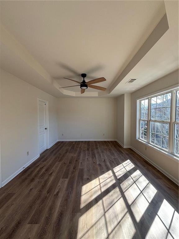 empty room with a tray ceiling, dark wood-type flooring, and ceiling fan