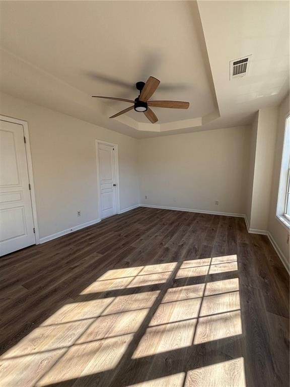 empty room featuring a raised ceiling, wood-type flooring, and ceiling fan