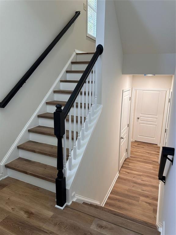 stairs with high vaulted ceiling and hardwood / wood-style floors