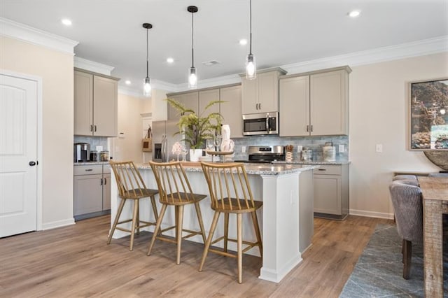 kitchen with a center island with sink, gray cabinets, stainless steel appliances, a kitchen bar, and light wood-type flooring