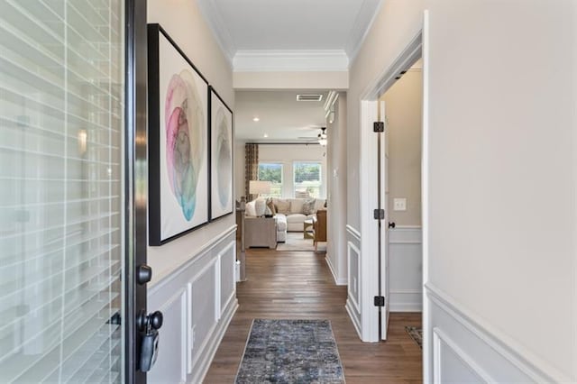 corridor featuring a wainscoted wall, visible vents, dark wood-style flooring, crown molding, and a decorative wall