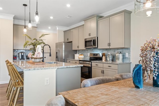 kitchen featuring an island with sink, gray cabinets, stainless steel appliances, and crown molding