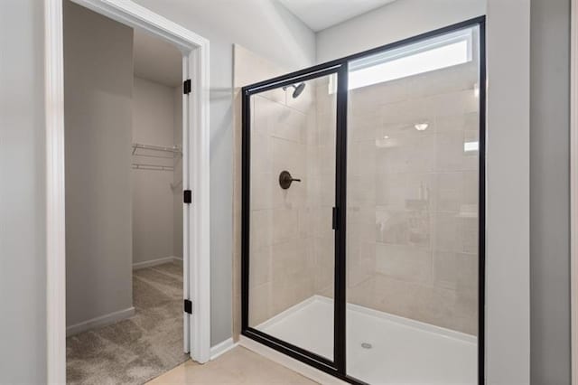 full bath with a walk in closet, baseboards, and a shower stall