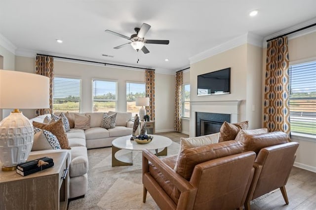 living area with plenty of natural light, light wood-style floors, a glass covered fireplace, and crown molding