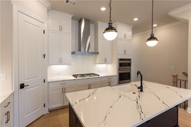 kitchen featuring pendant lighting, white cabinets, an island with sink, and wall chimney range hood