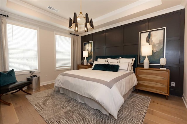 bedroom with an inviting chandelier, crown molding, a raised ceiling, and light wood-type flooring