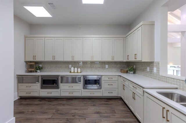 kitchen with decorative backsplash, stainless steel microwave, and dark hardwood / wood-style flooring