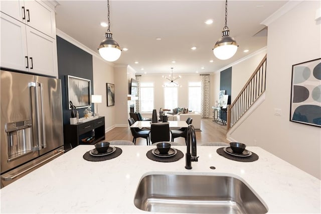 kitchen with high end fridge, decorative light fixtures, ornamental molding, and light stone countertops