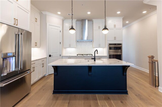 kitchen featuring white cabinets, stainless steel appliances, light hardwood / wood-style floors, wall chimney exhaust hood, and decorative light fixtures