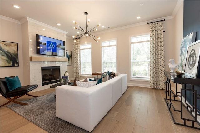 living room featuring an inviting chandelier, ornamental molding, a fireplace, and light wood-type flooring