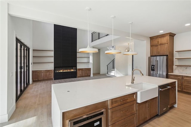 kitchen featuring an island with sink, appliances with stainless steel finishes, a large fireplace, hanging light fixtures, and sink