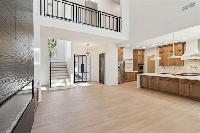 kitchen with decorative light fixtures, backsplash, light hardwood / wood-style floors, a high ceiling, and stainless steel appliances