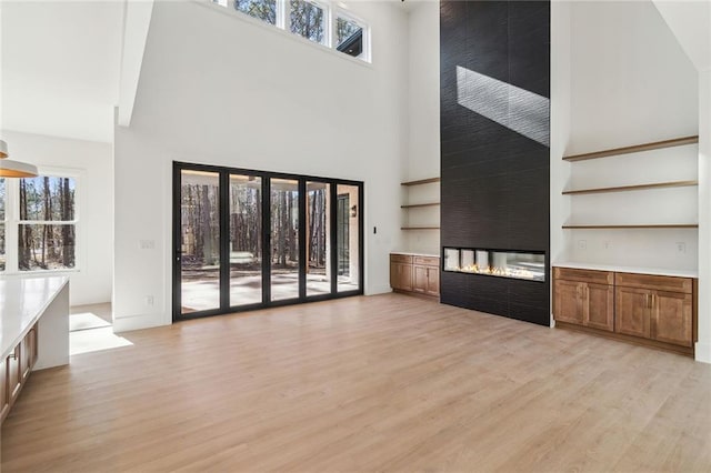 unfurnished living room featuring light wood-type flooring, a multi sided fireplace, and a high ceiling