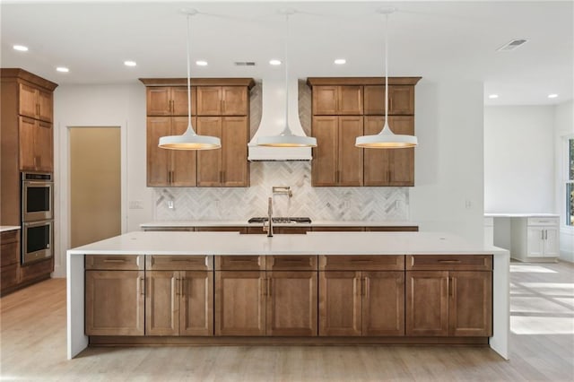 kitchen with premium range hood, appliances with stainless steel finishes, a center island with sink, and hanging light fixtures