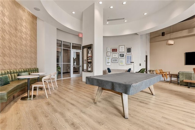 recreation room featuring pool table, a towering ceiling, and light hardwood / wood-style floors