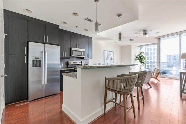 kitchen with a kitchen bar, a kitchen island, a wall of windows, and appliances with stainless steel finishes